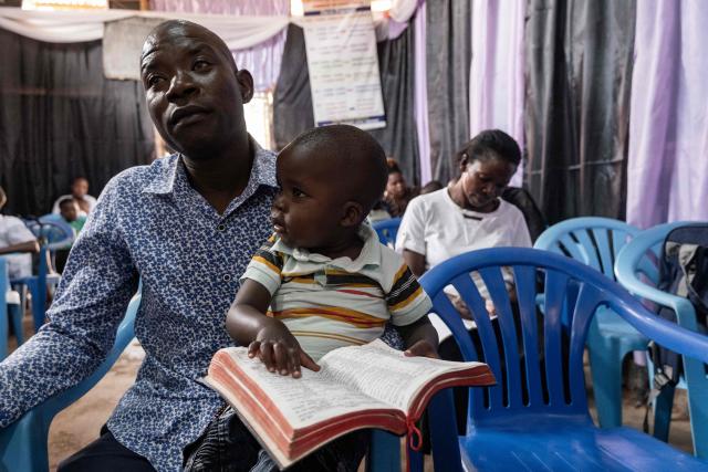 A man holds a baby as he opens the bible during a service for a peaceful election at Wakaliga Pentecostal Church in Kampala, on January 11, 2026, ahead of the 2026 Ugandan general election. (Photo by Badru Katumba / AFP)