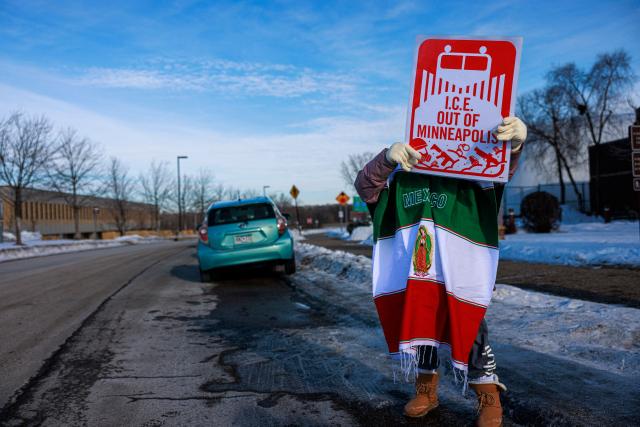 A protester wearing a Mexican flag holds a sign reading “ICE Out of Minneapolis” outside the Whipple Building, an ICE facility in Minneapolis, Minnesota, on January 11, 2026. A US Immigration and Customs Enforcement (ICE) agent shot and killed 37-year-old Renee Nicole Good on the streets of Minneapolis on January 7, leading to huge protests and outrage from local leaders who rejected White House claims she was a domestic terrorist. (Photo by Kerem YUCEL / AFP)