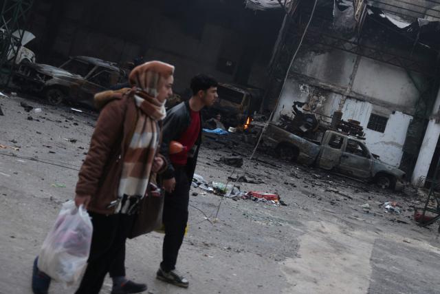 Citizens walk past destroyed vehicles following a ceasefire which ended several days of fighting between Syrian security forces and Kurdish fighters in the Kurdish-majority Sheikh Maqsud neighbourhood, of the northern city of Aleppo on January 11, 2026. Syria's Kurdish fighters said on January 11, 2026, that they agreed under a ceasefire to withdraw after days of fighting government forces in the city. The latest clashes erupted after negotiations to integrate the Kurds into the country's new government stalled. (Photo by Bakr ALkasem / AFP)