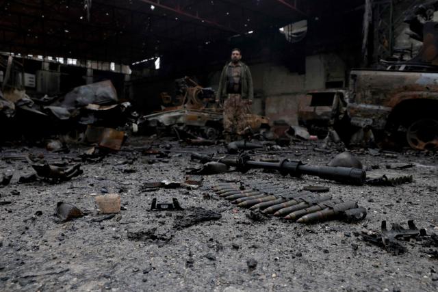A Syrian security officer stands next to munition strewn on the ground following a ceasefire which ended several days of fighting between Syrian security forces and Kurdish fighters in the Kurdish-majority Sheikh Maqsud neighbourhood, of the northern city of Aleppo on January 11, 2026. Syria's Kurdish fighters said on January 11, 2026, that they agreed under a ceasefire to withdraw after days of fighting government forces in the city. The latest clashes erupted after negotiations to integrate the Kurds into the country's new government stalled. (Photo by Bakr ALkasem / AFP)