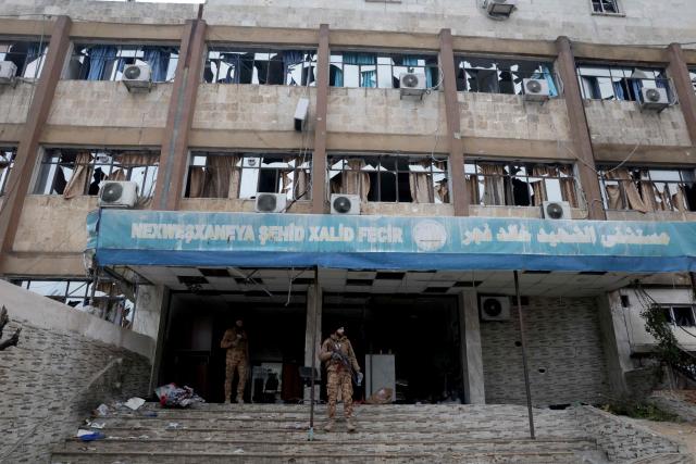 An armed Syrian security officer stands outside the Khaled Fajr Hospital, following a ceasefire which ended several days of fighting between Syrian security forces and Kurdish fighters in the Kurdish-majority Sheikh Maqsud neighbourhood, of the northern city of Aleppo on January 11, 2026. Syria's Kurdish fighters said on January 11, 2026, that they agreed under a ceasefire to withdraw after days of fighting government forces in the city. The latest clashes erupted after negotiations to integrate the Kurds into the country's new government stalled. (Photo by Bakr ALkasem / AFP)