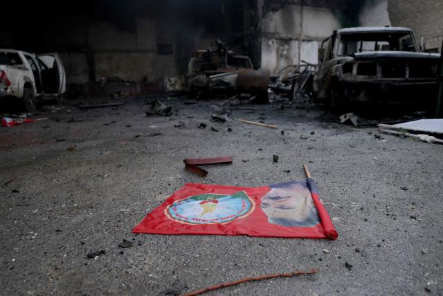 Destroyed vehicles and a flag with the image of jailed Kurdish leader Abdullah Ocalan, lies on the ground following a ceasefire which ended several days of fighting between Syrian security forces and Kurdish fighters in the Kurdish-majority Sheikh Maqsud neighbourhood, of the northern city of Aleppo on January 11, 2026. Syria's Kurdish fighters said on January 11, 2026, that they agreed under a ceasefire to withdraw after days of fighting government forces in the city. The latest clashes erupted after negotiations to integrate the Kurds into the country's new government stalled. (Photo by Bakr ALkasem / AFP)