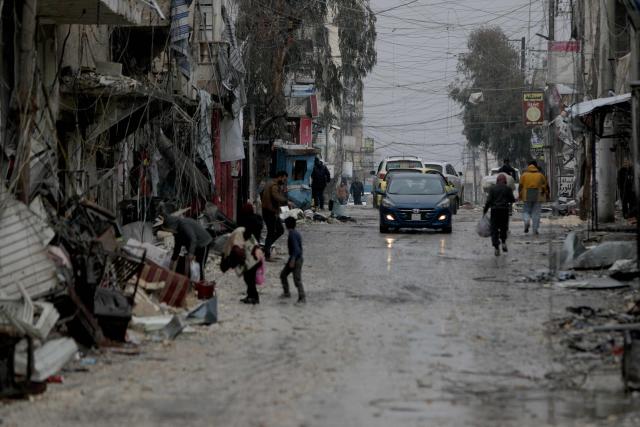 People walk down a street as a car drives by following a ceasefire which ended several days of fighting between Syrian security forces and Kurdish fighters in the Kurdish-majority Sheikh Maqsud neighbourhood, of the northern city of Aleppo on January 11, 2026. Syria's Kurdish fighters said on January 11, 2026, that they agreed under a ceasefire to withdraw after days of fighting government forces in the city. The latest clashes erupted after negotiations to integrate the Kurds into the country's new government stalled. (Photo by Bakr ALKASEM / AFP)