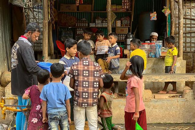 Rohingya refugee children surround a street vendor at the Kutupalong refugee camp in Ukhia on January 11, 2026. In Bangladesh's sprawling Rohingya camps of Cox's Bazar, where more than a million refugees forced to flee Myanmar live in squalid conditions, hope is a fragile but persistent force. In rows of bamboo shelters and muddy lanes, refugees who escaped Myanmar nearly a decade ago await developments more than 8,000 kilometres (5,000 miles) away at the International Court of Justice (ICJ) in The Hague, where a genocide case against Myanmar opens on January 12. (Photo by MH Mustafa / AFP) / TO GO WITH 'Bangladesh-Myanmar-Gambia-ICJ-Rohingya-Genocide' REPORTAGE