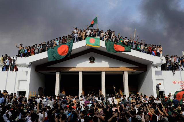 (FILES) Anti-government protestors display Bangladesh's national flag as they storm Prime Minister Sheikh Hasina's palace in Dhaka on August 5, 2024. After years of repression, Bangladesh's Islamist groups are mobilising ahead of February 12, 2026 elections, determined to gain a foothold in government as they sense their biggest opportunity in decades. At the centre of this formidable push is Jamaat-e-Islami, the country's largest and best-organised Islamist party. (Photo by K M ASAD / AFP)