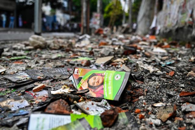 (FILES) A pamphlet featuring Bangladesh's ousted prime minister Sheikh Hasina lies over the charred remains of the Awami League party office, set on fire by anti-government protestors in Dhaka on August 6, 2024. Bangladesh has been in political turmoil since a student-led revolt overthrew Hasina in August 2024, ending her 15-year autocratic rule. The Muslim-majority nation of 170 million people will hold its first elections since the uprising on February 12, 2026. (Photo by Munir UZ ZAMAN / AFP)