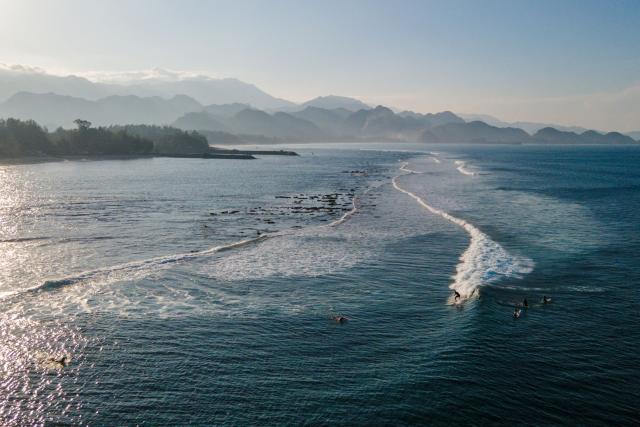 An aerial view shows a surfer riding a wave in Lhoknga beach, Indonesia's Aceh province on January 12, 2026. (Photo by CHAIDEER MAHYUDDIN / AFP)