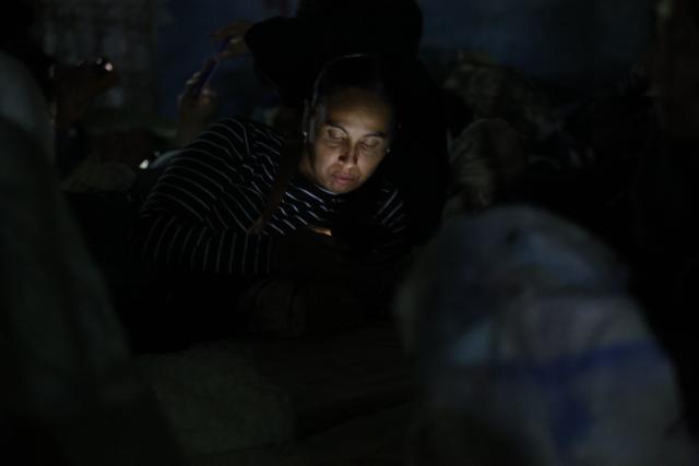 A woman checks her phone before sleeping on a mattress outside El Rodeo I prison in Guatire, Miranda State, some 30 kilometers east of Caracas on January 11, 2026. Venezuelans waited on January 11 for more political prisoners to be freed as ousted president Nicolas Maduro defiantly claimed from his US jail cell that he was "doing well" after being seized by US forces a week ago. (Photo by Pedro MATTEY / AFP)