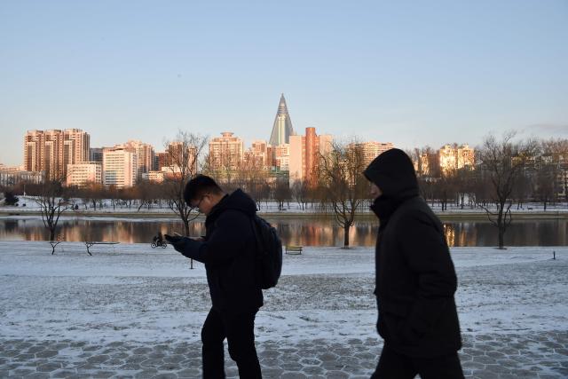 People walk along a snow-covered sidewalk in Pyongyang on January 12, 2026. (Photo by KIM Won Jin / AFP)