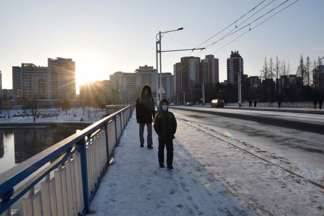 People walk along a snow-covered sidewalk on a bridge in Pyongyang on January 12, 2026. (Photo by KIM Won Jin / AFP)