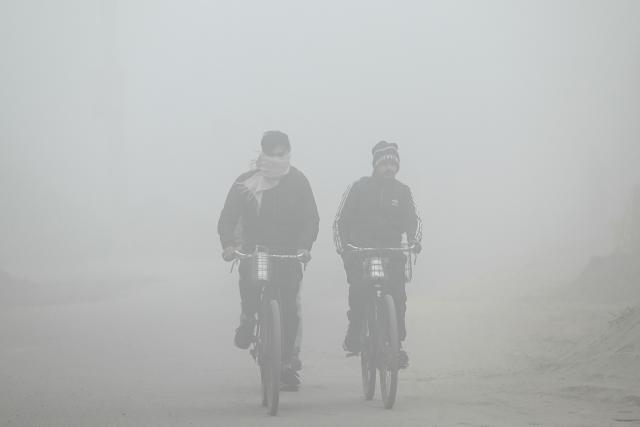 Labourers ride their bicycles amid dense fog on the outskirts of  Amritsar on January 12, 2026. (Photo by Narinder NANU / AFP)