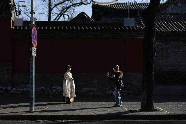 A woman wearing traditional clothes poses for a photo near the Forbidden City  in Beijing on January 12, 2026. (Photo by WANG Zhao / AFP)