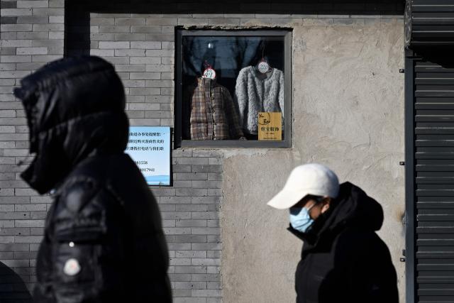 Pedestrians walk past a shop window displaying clothes for sale in Beijing on January 12, 2026. (Photo by WANG Zhao / AFP)
