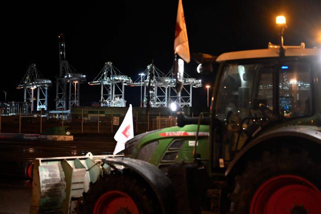 This photograph shows a tractor parked, as farmers stop truck drivers to inspect transport of foreign products, as part of national protests against the EU-Mercosur agreement and the government's handling of the contagious nodular dermatitis (CND) epidemic, on the harbour of Le Havre, northwestern France on January 12, 2026. (Photo by Lou BENOIST / AFP)