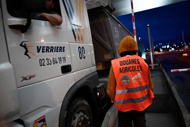 A French farmer wears a fake safety vest of Customs as farmers stop truck drivers to inspect transport of foreign products, as part of national protests against the EU-Mercosur agreement and the government's handling of the contagious nodular dermatitis (CND) epidemic, on the harbour of Le Havre, northwestern France on January 12, 2026. (Photo by Lou BENOIST / AFP)