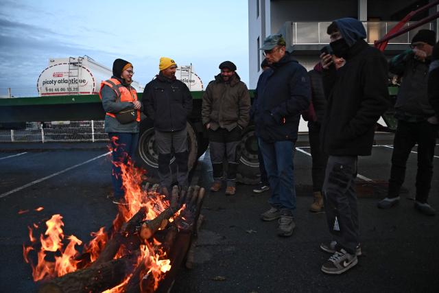 French farmers stand by a fire at the start of their blockade of an oil depot as part of national protests against the EU-Mercosur agreement and the government's handling of the contagious nodular dermatitis (CND) epidemic, on the harbour of La Pallice in La Rochelle, southwestern France on January 12, 2026. (Photo by Christophe ARCHAMBAULT / AFP)