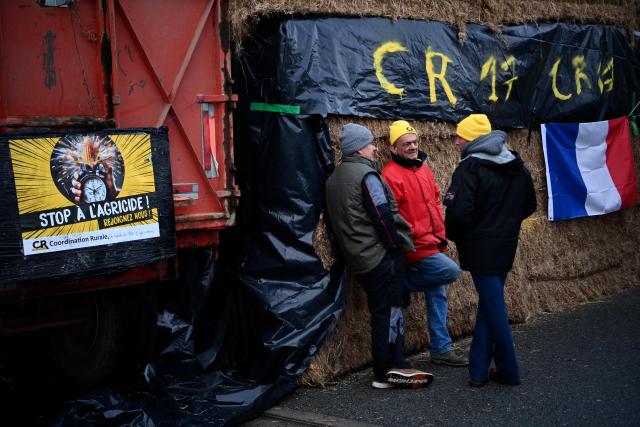 French farmers of the agricultural union Coordination Rurale (CR) talk in front of bales of straw during their blockade of an oil depot as part of national protests against the EU-Mercosur agreement and the government's handling of the contagious nodular dermatitis (CND) epidemic, on the harbour of La Pallice in La Rochelle, southwestern France on January 12, 2026. (Photo by Christophe ARCHAMBAULT / AFP)