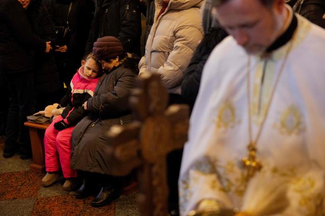 Relatives, friends and others mourn at the coffin of Sergiy Smolyak, a medic who died as a result of repeated Russian attacks, during the funeral ceremony at the St. Michael's Golden-Domed Monastery in Kyiv early on January 12, 2026, amid the Russian invasion of Ukraine. (Photo by Tetiana DZHAFAROVA / AFP)