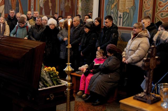 Relatives, friends and others mourn at the coffin of Sergiy Smolyak, a medic who died as a result of repeated Russian attacks, during the funeral ceremony at the St. Michael's Golden-Domed Monastery in Kyiv early on January 12, 2026, amid the Russian invasion of Ukraine. (Photo by Tetiana DZHAFAROVA / AFP)