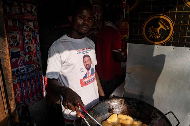 A supporter of opposition leader and presidential candidate for the National Unity Platform (NUP) Robert Kyagulanyi Ssentamu, popularly known as Bobi Wine, wears a t-shirt bearing Wine's face, as he cooks food in a stall during a final campaign rally in Kampala, on January 12, 2026. (Photo by Badru Katumba / AFP)