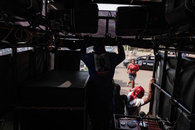 A pedestrian runs in the street as supporters of opposition leader and presidential candidate for the National Unity Platform (NUP) Robert Kyagulanyi Ssentamu, popularly known as Bobi Wine, use a sound system on a truck, to call his supporters to attend his final campaign rally in Kampala, on January 12, 2026. (Photo by Badru Katumba / AFP)