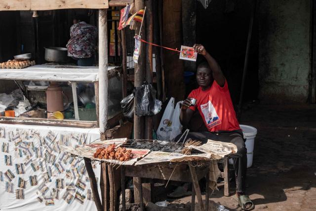 A man at a food stall shows a tag bearing the image of opposition leader and presidential candidate for the National Unity Platform (NUP) Robert Kyagulanyi Ssentamu, popularly known as Bobi Wine, in Kampala, on January 12, 2026. (Photo by Badru Katumba / AFP)