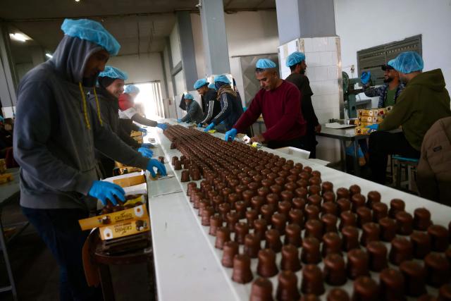 Palestinian workers box sweets locally known as "al-Shatwi" (Winter) Crimbo sweets, as the Al-Arees factory gradually resumes operations after a hiatus caused by the Gaza war which led to shortages of raw materials used in their products, in Deir al-Balah, in the central Gaza Strip on January 12, 2026, following a US-brokered truce that halted the two-year war. (Photo by Bashar Taleb / AFP)