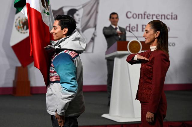 Mexico's President Claudia Sheinbaum (R) and figure skater Donovan Carrillo salute the Mexican flag during the flag-raising ceremony for the Mexican delegation of athletes that will participate in the Milano-Cortina 2026 Winter Olympic Games, after her daily press conference at the National Palace in Mexico City on January 12, 2026. (Photo by Alfredo ESTRELLA / AFP)