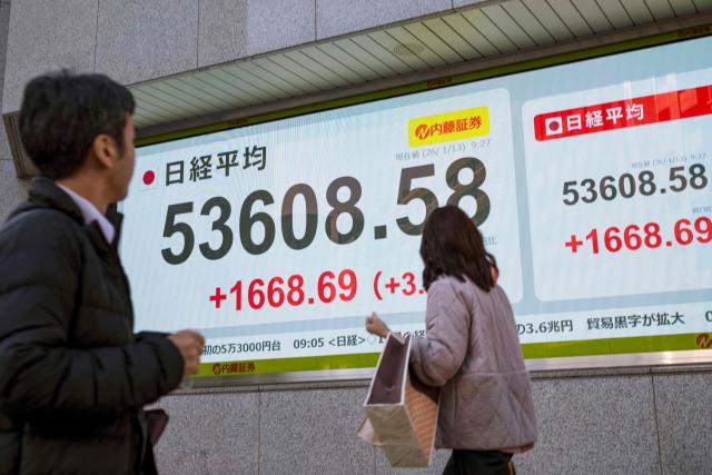 Pedestrians walk in front of an electronic quotation board displaying the Nikkei 225 stock prices on the Tokyo Stock Exchange in Tokyo on January 13, 2026. (Photo by Kazuhiro NOGI / AFP)