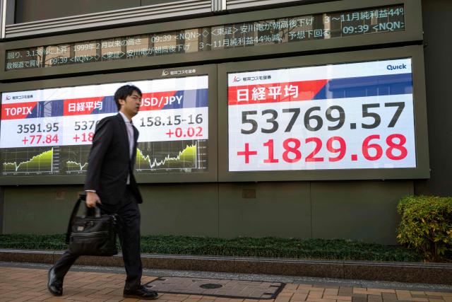 A man walks past an electronic quotation board displaying numbers of the Nikkei Stock Average (R) on the Tokyo Stock Exchange in Tokyo on January 13, 2026. (Photo by Kazuhiro NOGI / AFP)