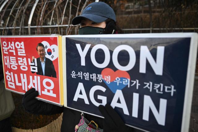A supporter of South Korea's impeached former president Yoon Suk Yeol holds a placard showing a picture of Yoon in front of the Seoul Central District Court in Seoul on January 13, 2026, as Yoon's final criminal trial on insurrection charges is scheduled to be held in the court. (Photo by Jung Yeon-je / AFP)