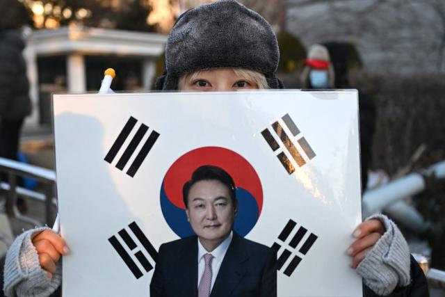 A supporter of South Korea's impeached fprmer president Yoon Suk Yeol holds a placard showing a picture of Yoon in front of the Seoul Central District Court in Seoul on January 13, 2026, as Yoon's final criminal trial on insurrection charges is scheduled to be held in the court. (Photo by Jung Yeon-je / AFP)