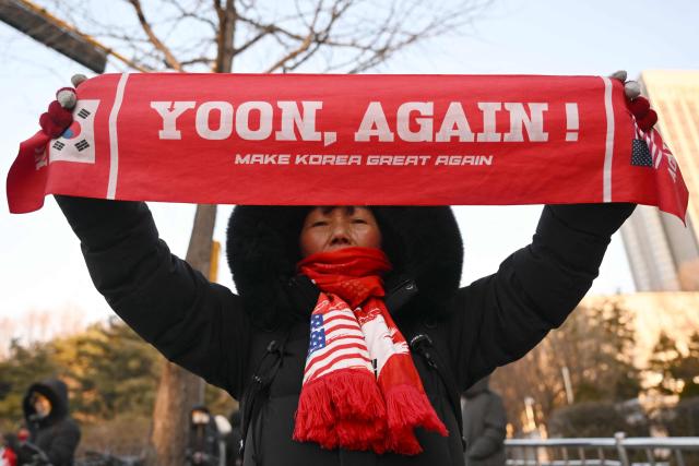 A supporter of South Korea's impeached former president Yoon Suk Yeol holds up a banner reading "Yoon, Again!" in front of the Seoul Central District Court in Seoul on January 13, 2026, as Yoon's final criminal trial on insurrection charges is scheduled to be held in the court. (Photo by Jung Yeon-je / AFP)