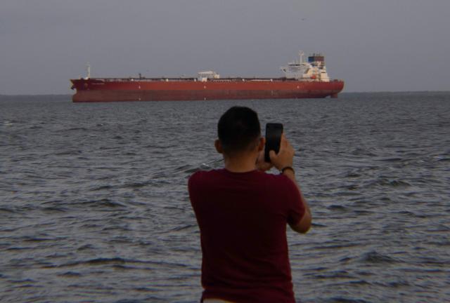 A man takes pictures of a crude oil tanker at Maracaibo Lake in Maracaibo, Venezuela, on January 12, 2026. After the US raid that deposed Nicolas Maduro as Venezuela's leader, citizens hope the ensuing talks on selling its oil to US may improve their dire economic fortunes. (Photo by Margioni BERMÚDEZ / AFP)