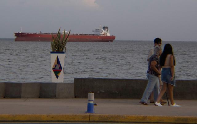 People walk in front of a crude oil tanker at Maracaibo Lake in Maracaibo, Venezuela, on January 12, 2026. After the US raid that deposed Nicolas Maduro as Venezuela's leader, citizens hope the ensuing talks on selling its oil to US may improve their dire economic fortunes. (Photo by Margioni BERMÚDEZ / AFP)