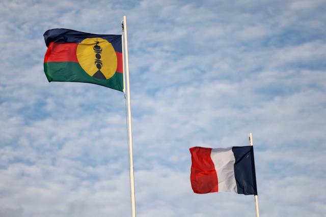 (FILES) The New Caledonia flag (L) flutters in the wind beside the French flag in Noumea on July 24, 2023 ahead of the arrival of France's President Emmanuel Macron on his visit to New Caledonia. Caledonian independence movement, the Kanak and Socialist National Liberation Front (FLNKS), announced on January 13, 2026, that it would not attend the meeting on the institutional future of the archipelago organised by the French president at the Elysee Palace on January 16, 2026. (Photo by Ludovic MARIN / AFP)