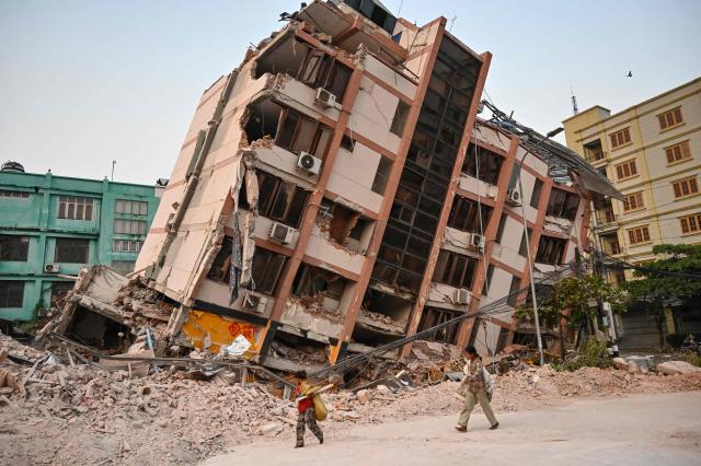 (FILES) Children walk past a collapsed building in Mandalay on April 2, 2025, five days after a major earthquake struck central Myanmar. Global natural disaster losses dropped sharply to $224 billion in 2025, reinsurer Munich Re said on January 13, 2026, but warned of a still "alarming" picture of extreme weather events driven by climate change. (Photo by AFP)