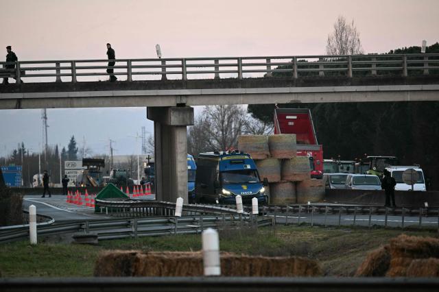 French gendarmes look at tractors and farmers on the A64 motorway during a farmers' blockade to protest against the government's mandatory culling protocol for cattle herds affected by lumpy skin disease (dermatose nodulaire contagieuse) and the EU-Mercosur trade deal, in Carbonne, southwestern France on January 13, 2026. A roadblock that farmers have been maintaining for a month on the A64 motorway near Toulouse was being dismantled in the morning of January 13, 2026 by law enforcement, according to multiple sources. (Photo by Lionel BONAVENTURE / AFP)