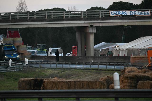 French gendarmes stand beside tractors and farmers on the A64 motorway during a farmers' blockade to protest against the government's mandatory culling protocol for cattle herds affected by lumpy skin disease (dermatose nodulaire contagieuse) and the EU-Mercosur trade deal, in Carbonne, southwestern France on January 13, 2026. A roadblock that farmers have been maintaining for a month on the A64 motorway near Toulouse was being dismantled in the morning of January 13, 2026 by law enforcement, according to multiple sources. (Photo by Lionel BONAVENTURE / AFP)