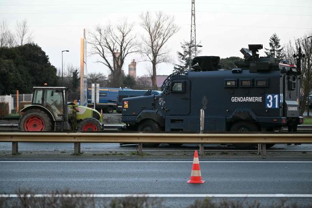 A photo shows a French gendarmerie Centaure armoured vehicle next to a tractor on the A64 motorway during a farmers' blockade to protest against the government's mandatory culling protocol for cattle herds affected by lumpy skin disease (dermatose nodulaire contagieuse) and the EU-Mercosur trade deal, in Carbonne, southwestern France on January 13, 2026. A roadblock that farmers have been maintaining for a month on the A64 motorway near Toulouse was being dismantled in the morning of January 13, 2026 by law enforcement, according to multiple sources. (Photo by Lionel BONAVENTURE / AFP)