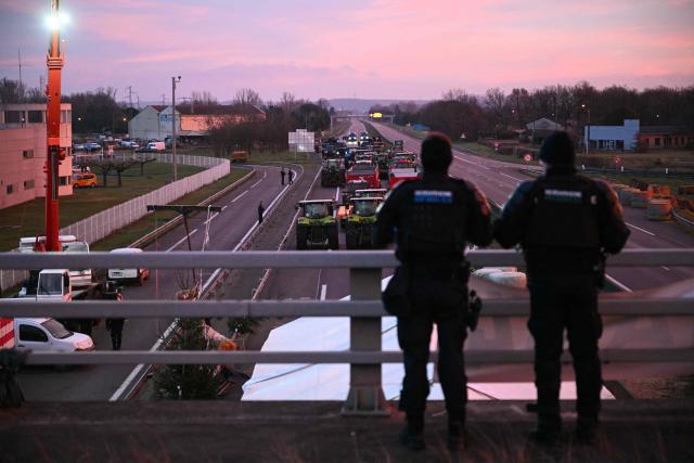 French gendarmes look at tractors and farmers on the A64 motorway during a farmers' blockade to protest against the government's mandatory culling protocol for cattle herds affected by lumpy skin disease (dermatose nodulaire contagieuse) and the EU-Mercosur trade deal, in Carbonne, southwestern France on January 13, 2026. A roadblock that farmers have been maintaining for a month on the A64 motorway near Toulouse was being dismantled in the morning of January 13, 2026 by law enforcement, according to multiple sources. (Photo by Lionel BONAVENTURE / AFP)