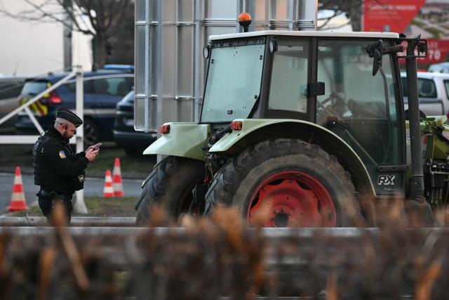 A French gendarme takes a picture of a tractor plate on the A64 motorway during a farmers' blockade to protest against the government's mandatory culling protocol for cattle herds affected by lumpy skin disease (dermatose nodulaire contagieuse) and the EU-Mercosur trade deal, in Carbonne, southwestern France on January 13, 2026. A roadblock that farmers have been maintaining for a month on the A64 motorway near Toulouse was being dismantled in the morning of January 13, 2026 by law enforcement, according to multiple sources. (Photo by Lionel BONAVENTURE / AFP)