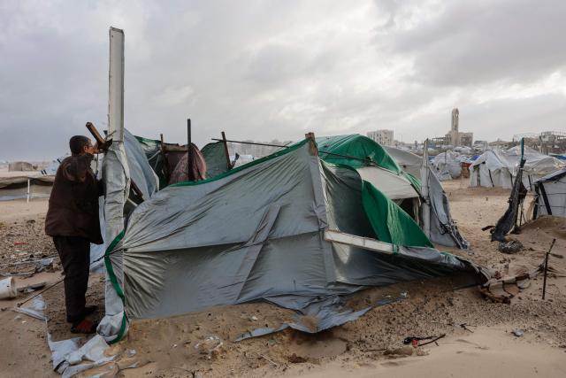 A displaced Palestinian man fixes a tent shelter set up along the shore in Gaza City as strong winter winds sweep the Palestinian enclave on January 13, 2026. A fragile ceasefire has been in place since October, following a deadly war waged by Israel in response to Hamas's unprecedented October 7, 2023 attack on Israel. Nearly 80 percent of buildings in Gaza have been destroyed or damaged by the war, according to UN data. (Photo by Omar AL-QATTAA / AFP)