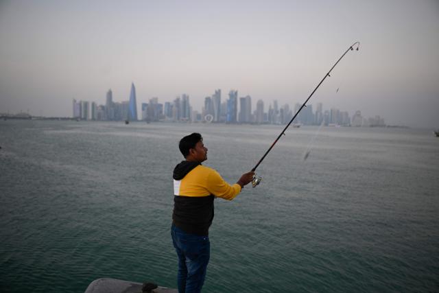 A man casts a fishing rod at the corniche overlooking the city skyline in Doha on January 13, 2026. (Photo by Mahmud HAMS / AFP)