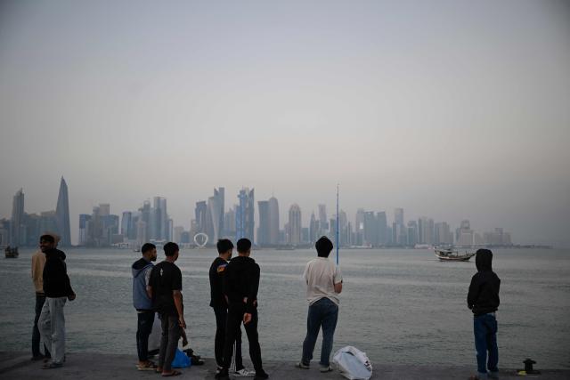 Men watch as another use a fishing to catch fish at the corniche overlooking the city skyline in Doha on January 13, 2026. (Photo by Mahmud HAMS / AFP)