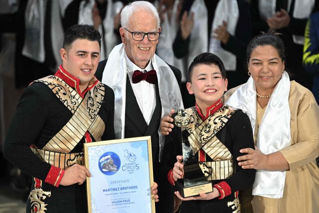Gold trophy winner Columbian and Japanese acrobats, members of the 'Martinez Brothers', pose with their Gold trophy at the 16th Budapest International Circus Festival on stage of the Capital Grand Circus in Budapest during the awarding ceremony of the festival in Budapest, on January 12, 2026, with (2nd L) the honorary chairman of the jury Swiss Eugene Chaplin and President of Peru's first international circus festival Maria Teresa Chirinos Versace (R). This festival is the second-largest professional circus arts event globally, ranking just behind the International Circus Festival of Monte-Carlo. (Photo by Attila KISBENEDEK / AFP)