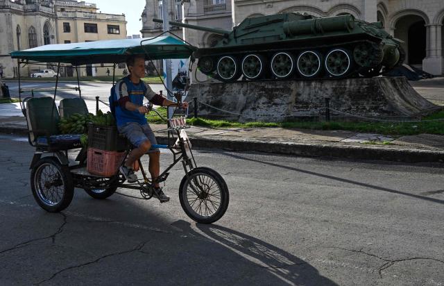 A man on his bicycle taxi passes in front of a Soviet-era SU-85 assault gun, used by Cuban leader Fidel Castro to fire on the American ship Houston during the mercenary invasion of Playa Giron (Bay of Pigs) in April 1961, on display outside the Museum of the Revolution in Havana on January 13, 2026. (Photo by YAMIL LAGE / AFP)