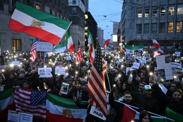 Anti-Iranian regime protesters hold pre-1979 Islamic Revolution Iranian flags, US flags and light their cellphones during a gathering outside the US Consulate in Milan, on January 13, 2026. (Photo by Piero CRUCIATTI / AFP)