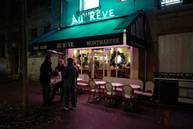 TOPSHOT - Customers stand outside of Au Reve bar cafe in Montmartre district of Paris on December 17, 2025. France's President argued on January 5, 2026 for the inclusion of French bistros and cafes in UNESCO's intangible cultural heritage, alongside the baguette. The French Bistros and Cafes Association launched an initiative in 2024 to have these convivial places listed as UNESCO World Heritage sites. "The bistros and cafes of France are keepers of time. They cross centuries and intersect generations," it emphasizes on its website. (Photo by Ludovic MARIN / AFP)