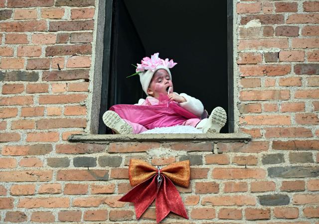 A young girl sits in a window during a carnival procession through the village of Vevcani, south-western Macedonia, on January 13, 2026. The carnival, which is over 1400 years old, is held every year on the eve of the feast of Saint Basil, which also marks the beginning of the New Year according to the Julian calendar and observed by the Macedonian Orthodox Church. (Photo by Robert ATANASOVSKI / AFP)